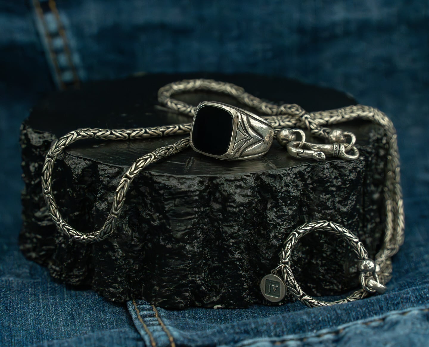 Silver jewelry set on dark, textured surface.